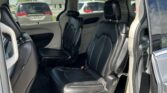Interior of a vehicle with black leather seats and captain chairs, beige trim, and an open rear door showing the outside parking lot with other cars.