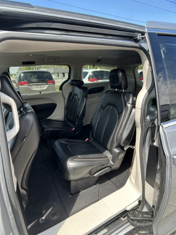 Interior of a vehicle with black leather seats and captain chairs, beige trim, and an open rear door showing the outside parking lot with other cars.