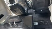 Minivan interior with black leather seats, third-row folded forward, showing spacious cargo area and gray carpet.