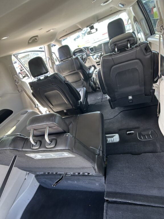 Minivan interior with black leather seats, third-row folded forward, showing spacious cargo area and gray carpet.