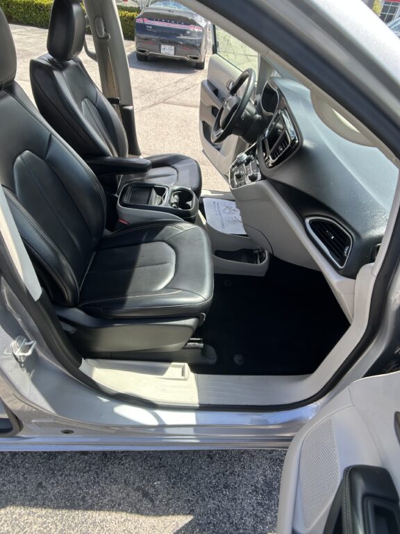 Open-door view of a car interior with black leather front seats, center console, and dashboard controls.