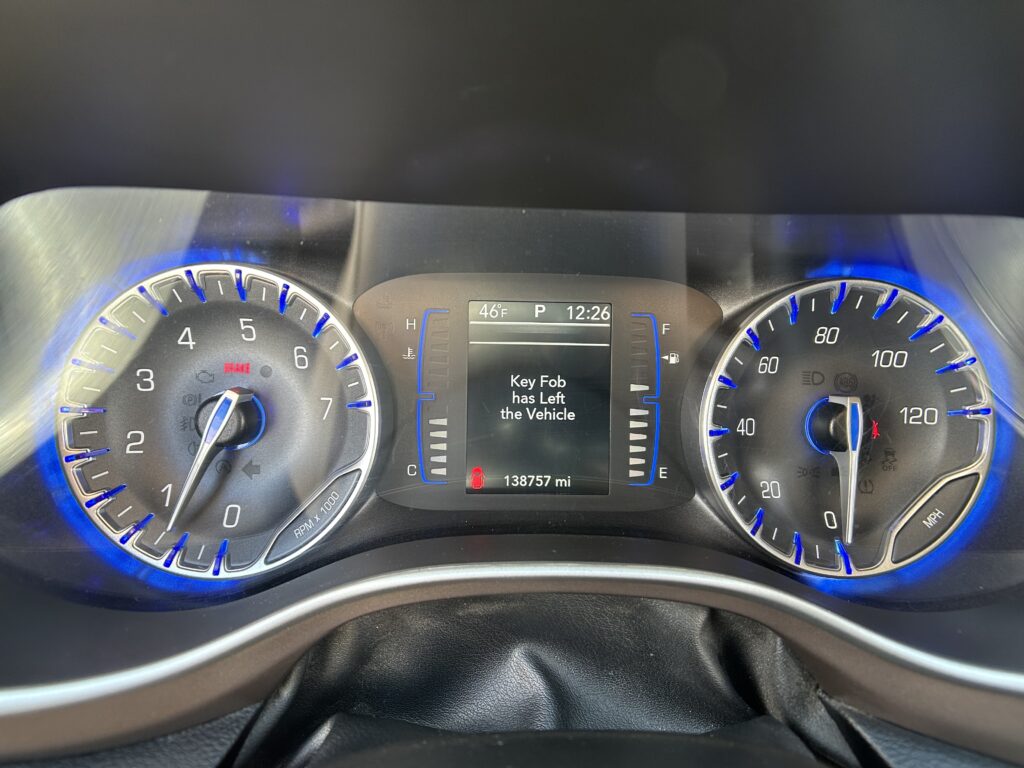 Vehicle dashboard with blue-lit analog gauges on left and right, center display shows 'Key Fob has Left the Vehicle' and 138,757 mi total miles.