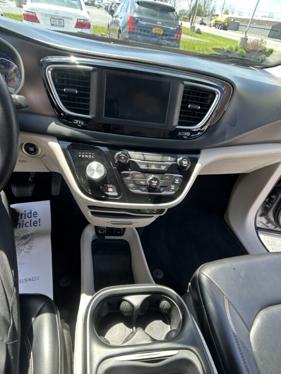 Driver's view of the car’s center console: touchscreen display flanked by air vents, climate controls, and gear selector with cupholders nearby.