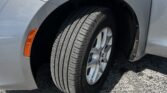 Front left wheel of a silver car, showing the tire, alloy rim, and wheel well with an orange side marker light beside the fender on asphalt.