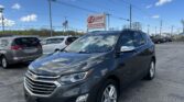 Grey Chevrolet SUV foreground in a car lot with an E-Z LOAN Auto Sales sign and blue sky overhead.