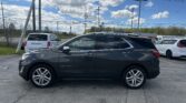 Gray Chevrolet Equinox parked in a lot, with power lines and a blue sky with clouds overhead, and cracked pavement in the foreground