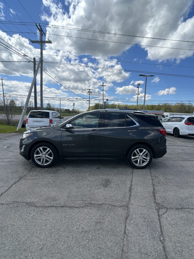 Gray Chevrolet Equinox parked in a lot, with power lines and a blue sky with clouds overhead, and cracked pavement in the foreground