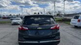 Rear view of a dark gray Chevrolet Equinox in a parking lot with other cars and a blue sky full of clouds.