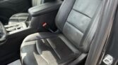 Front interior of a car showing black leather front seats, center console, and door panel with stitching detail.