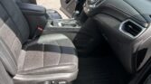 Front interior of a black Chevrolet Equinox with the driver's door open, showing steering wheel, center console, and dashboard; dealership lot visible outside.