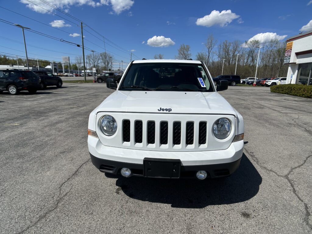 Front view of a white Jeep in a car dealership lot on a sunny day.
