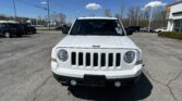 Front view of a white Jeep in a car dealership lot on a sunny day.