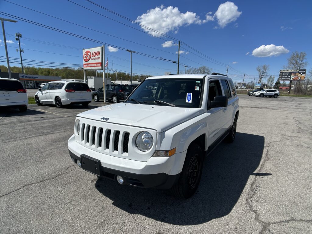 White Jeep SUV in a car dealership lot with other vehicles and an EZ Loan Auto Sales sign in the background under a clear blue sky.