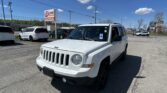 White Jeep SUV in a car dealership lot with other vehicles and an EZ Loan Auto Sales sign in the background under a clear blue sky.