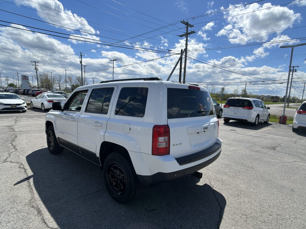 White Jeep SUV parked in a dealership lot with other cars, under a blue sky with power lines overhead.