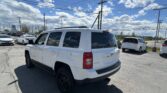White Jeep SUV parked in a dealership lot with other cars, under a blue sky with power lines overhead.