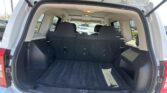 Open rear hatch of a white SUV showing an empty cargo area with black carpeting and folded third-row seats visible at the back of the cabin.