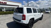 White Jeep SUV parked in a dealership lot beside a building with a red 'SALES' sign under a blue sky.