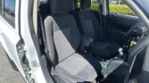 Front seats of a car interior with black fabric upholstery, visible seat belts, and center console, door open to the outside parking lot.