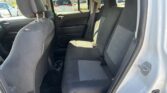 Rear interior of a gray SUV showing two rows of black cloth seats, cup holders, and a view of parked cars outside through the windows.