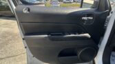 Interior of a vehicle door with a chrome door handle, black plastic panel, and window controls; parking lot visible outside the window.