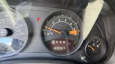 Close-up of car dashboard showing speedometer, tachometer, gear selector in Park, and a red seatbelt warning light.
