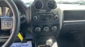 View of a car interior from the driver's seat: steering wheel on the left, center dashboard with two round air vents, radio controls, climate knobs, and a gear shifter; a paper on the floor reads 'We Take Pride In Your Vehicle' (sunlit windshield).