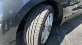 Close-up of a blue SUV's front left wheel, tire, and fender with reflected surroundings visible on the body.