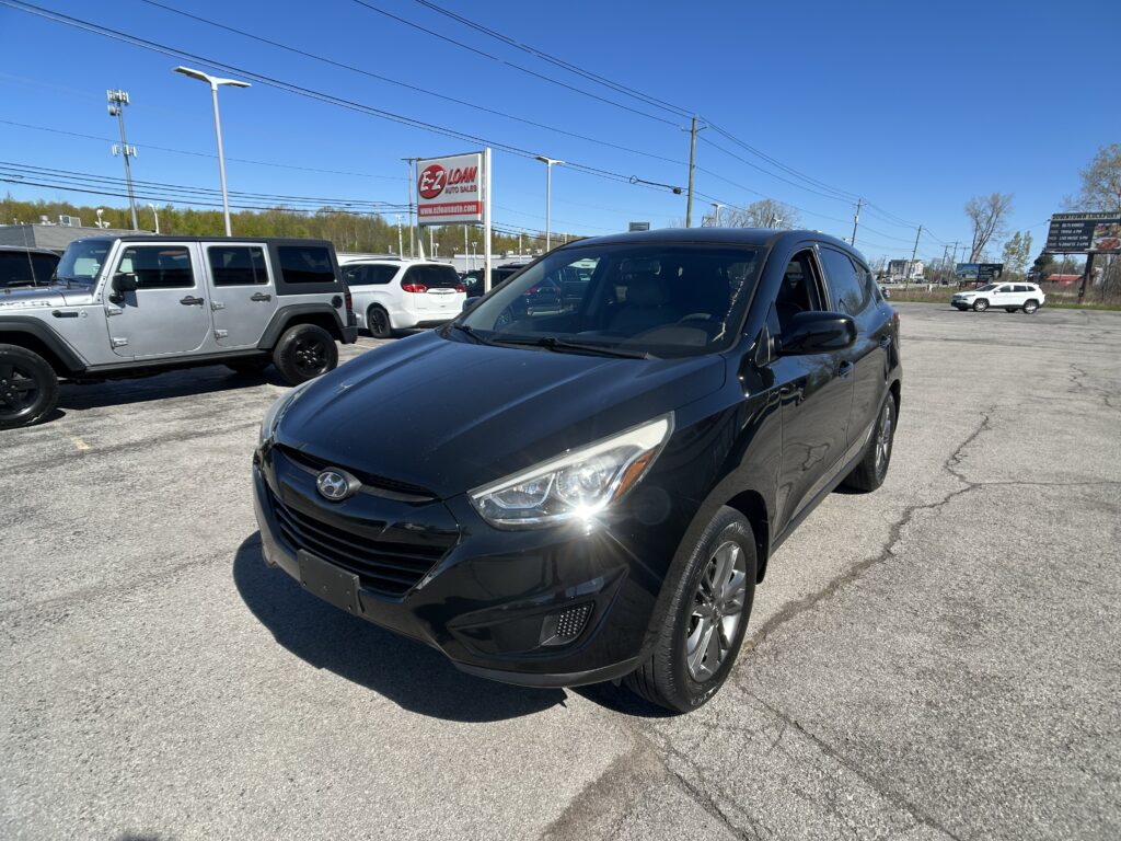 Black Hyundai SUV in the foreground at a sunny car dealership lot.