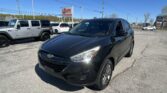 Black Hyundai SUV in the foreground at a sunny car dealership lot.