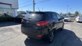 Black Hyundai SUV in the foreground at a car dealership lot with other cars and a white building on the left under a clear blue sky.