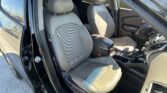 Inside a car: gray fabric front seats, center console, steering wheel, and an open driver’s door.