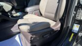 Interior view of a car showing the front passenger seat and center console with beige fabric upholstery; the driver’s door is open and safety labels are visible on the door frame in bright sunlight.