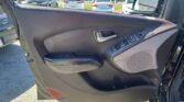 Close-up of a car's driver-side door interior with window controls and door handle; a parking lot of white cars is visible outside the window.