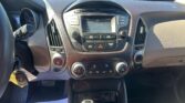 Dashboard center console with radio displaying 106.5 FM and climate controls, view through windshield of a car in a dealership lot