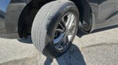 Close-up of a car wheel and tire, showing the tread pattern and alloy rim inside a dark wheel well on asphalt surface