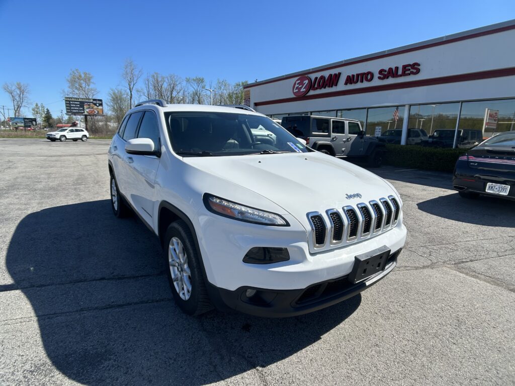 White Jeep SUV in the dealership lot with EZ Loan Auto Sales signage on the building and a clear blue sky above.