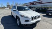 White Jeep SUV in the dealership lot with EZ Loan Auto Sales signage on the building and a clear blue sky above.