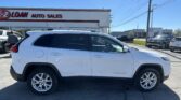 White Jeep Cherokee SUV parked in a dealership lot with the 'E-Z LOAN AUTO SALES' sign visible in the background, under a clear blue sky.