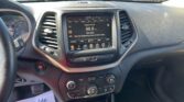 Interior of a car dashboard showing a touchscreen infotainment system and climate controls, with papers on the passenger side floor reading promotional text.