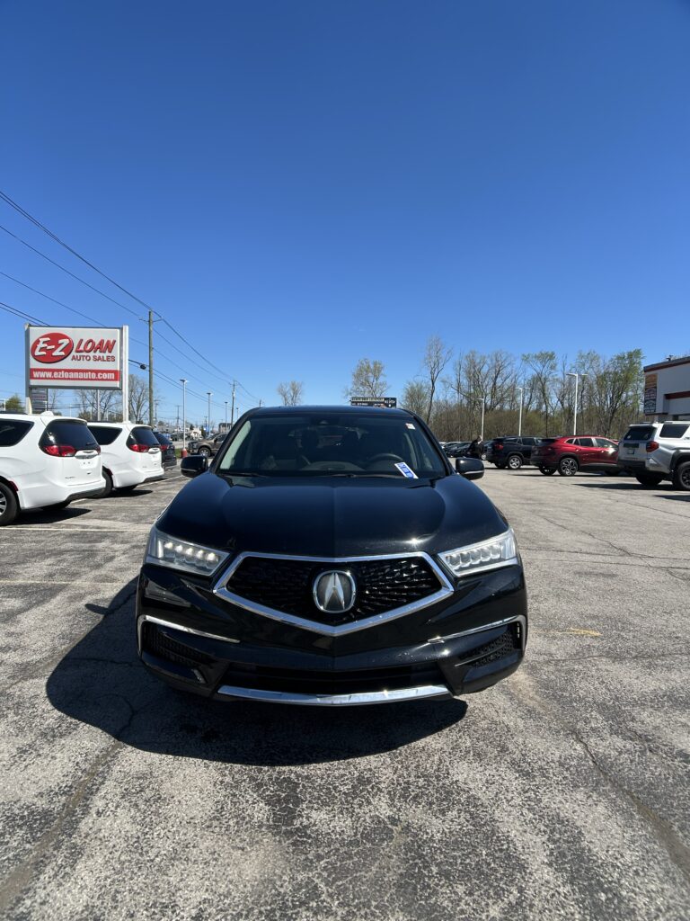 Front view of a black Acura SUV in a car lot with an EZ Loan Auto Sales sign to the left and other vehicles in the background, under a clear blue sky.
