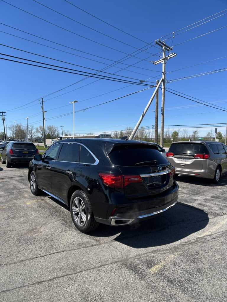 Rear three-quarter view of a black Mercedes SUV parked in a lot, with tall power lines and a utility pole against a clear blue sky.