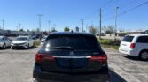 Rear view of a black Acura MDX parked in a lot, with other cars and overhead power lines against a blue sky.