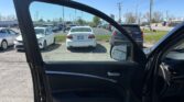 Open car door frame in the foreground with a parking lot of cars and a clear blue sky in the background, viewed from inside the car.