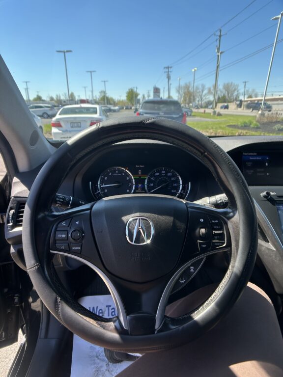 Driver's view from the seat showing the steering wheel and dashboard, with traffic ahead on a sunny road through the windshield.