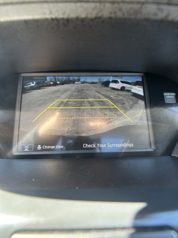 Car rear-view camera display showing parking guidelines (yellow lines) and a note to check surroundings.
