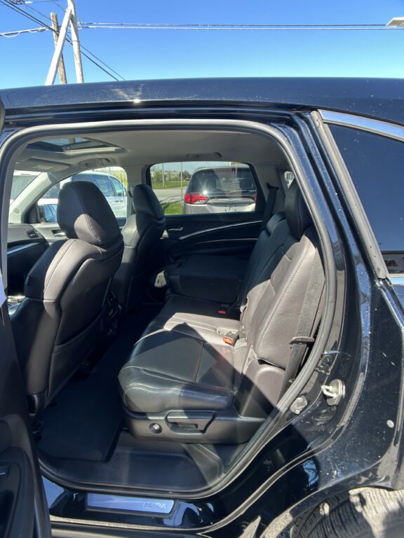 Rear passenger area of a black Acura SUV with the rear door open, showing black leather seats and center console area.