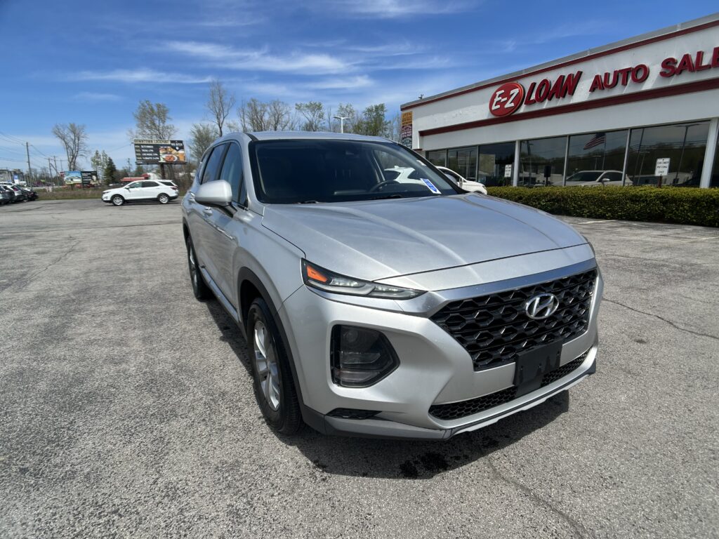 Silver Hyundai SUV in a dealership lot, in front of an EZ LOAN Auto Sales building on a sunny day