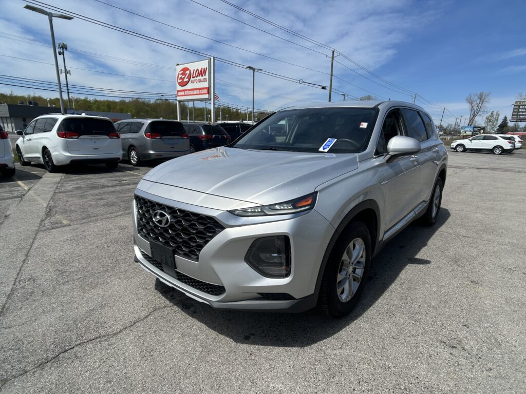 Silver SUV in the foreground at a car dealership lot, with multiple other cars and an E-Z LOAN Auto Sales sign in the background.