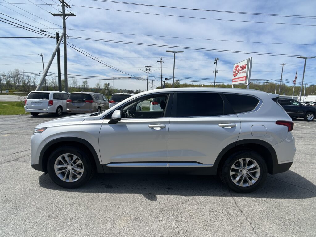 Silver SUV in the foreground at a car dealership lot, with other vans and a large EZ LOAN Auto Sales sign in the background.